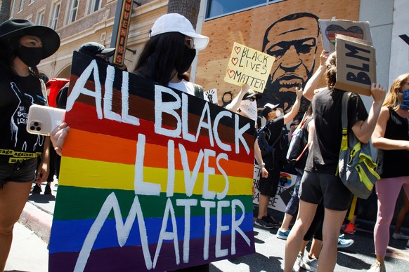 epa08485575 All Black Lives Matter protesters hold rainbow-colored signs near a mural of George Floyd during their solidarity march with the LGBT movement outside the TCL Chinese Theatre on Hollywood  ...