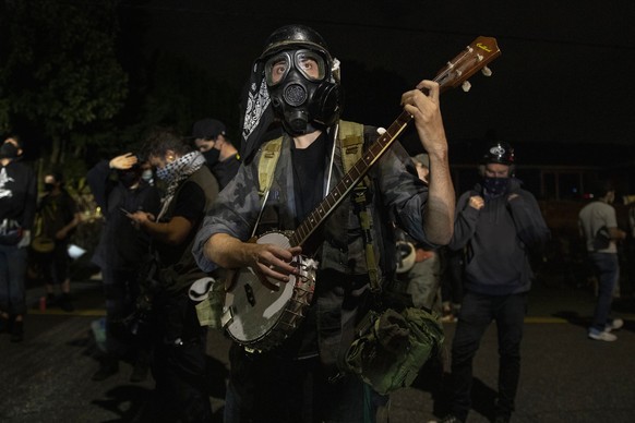 A protester plays a banjo during the nightly protests at a Portland police precinct on Sunday, Aug. 30, 2020 in Portland, Ore. Oregon State Police will return to Portland to help local authorities aft ...