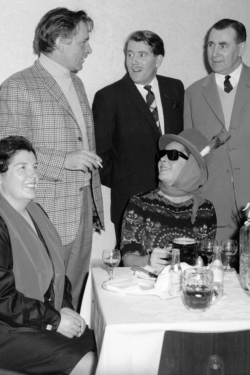 ritish-born American actress Elizabeth Taylor, dressed in a colorful sports outfit, looks up from her pint of beer as her husband, Welsh actor Richard Burton, talks to friends on Jan. 16, 1965 in Card ...