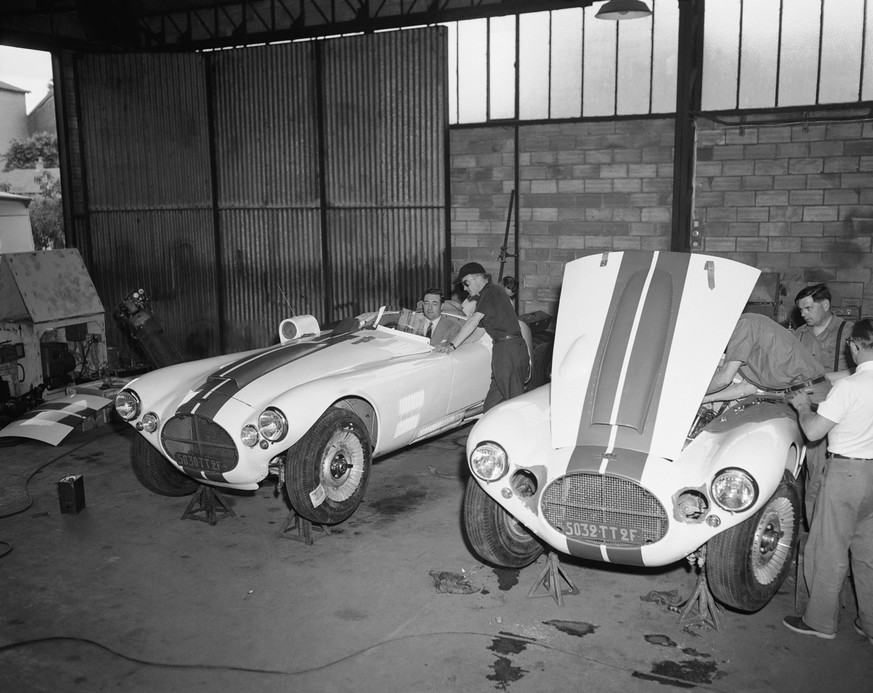 Briggs Cunningham (left) of Green Farms, Connecticut, sits at the wheels of one of his team of three Cunningham sports cars as he talks with one of his drivers, Fred Whacker of Chicago, Illinois in a  ...
