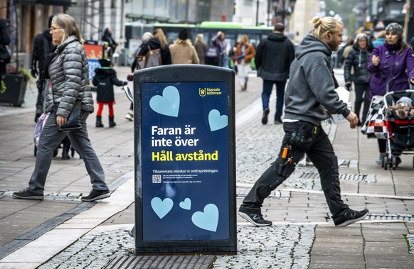 People pass a trash can with a sign reading &quot;The danger is not over - Keep your distance&quot; in a pedestrian street in central Uppsala, Sweden, Wednesday, Oct. 21, 2020. Uppsala, a university c ...