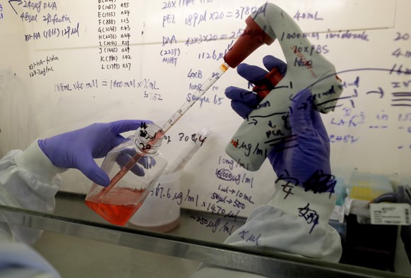 FILE - In this July 30, 2020 file photo, Kai Hu, a research associate transfers medium to cells, in the laboratory at Imperial College in London. Imperial College is working on the development of a CO ...