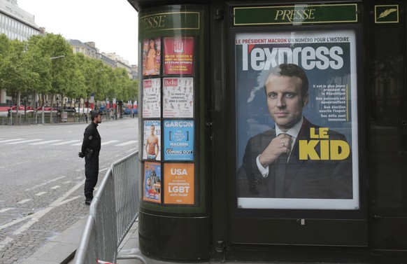 A police officer stands guard next to a newsstand displaying the cover of a news magazine depicting French president-elect Emmanuel Macron during a ceremony to mark the end of World War II on the Cham ...
