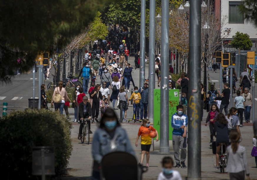 Families with their children walk along a boulevard in Barcelona, Spain, Sunday, April 26, 2020 as the lockdown to combat the spread of coronavirus continues. On Sunday, children under 14 years old wi ...