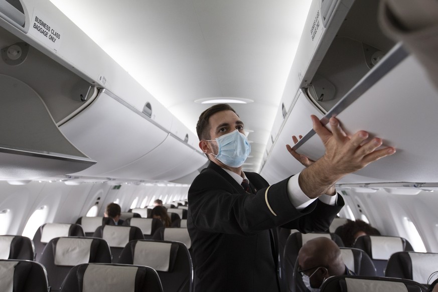 epa08486922 A cabin crew member of Swiss International Air Lines, wearing a face mask, prepares the aircraft prior to departure to London at the Geneva Airport, in Geneva, Switzerland, 15 June 2020. F ...
