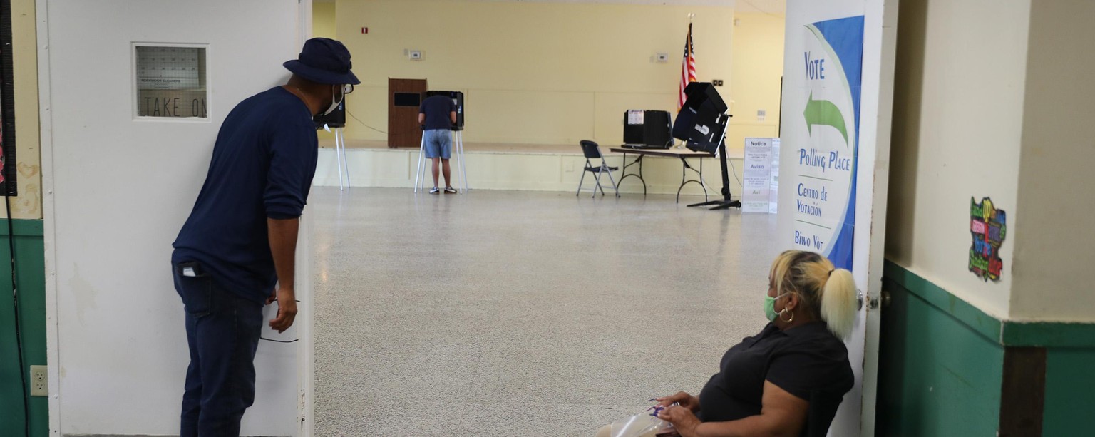 MIAMI, FLORIDA - AUGUST 18: Poll workers look on as a voter fills out his ballot on primary election day on August 18, 2020 in Miami, Florida. Voters are casting ballots in Miami-Dade to elect Miami-D ...
