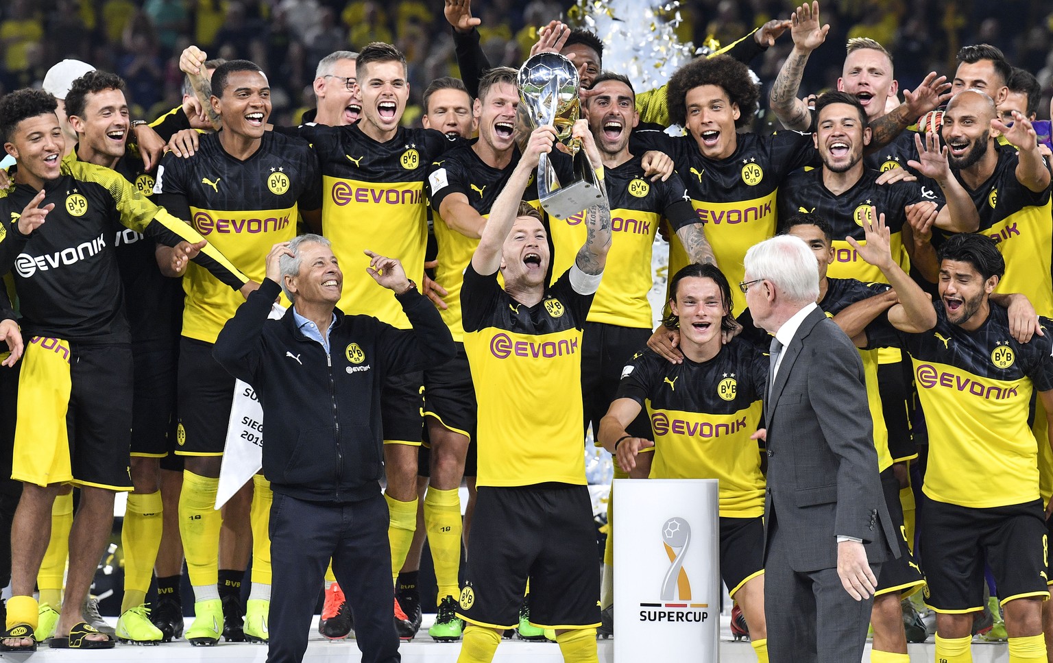 Dortmund&#039;s Marco Reus lifts up the trophy beside head coach Lucien Favre, left, and Dortmund&#039;s President Reinhard Rauball, right, as he celebrates with teammates after winning the German Sup ...