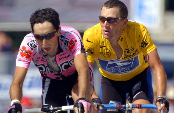Joseba Beloki of Spain, left, crosses the finish line while Lance Armstrong of Austin, Texas, right, looks at a clock indicating the time lapsed after the winner of the stage Santiago Botero of Colomb ...