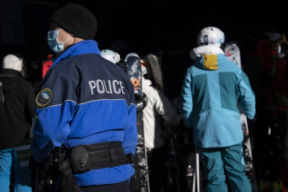 Un policier municipal de Bagnes distribue des masques de protection a des skieurs qui font la queue suite a un arret momentane de la telecabine sur le domaine skiable valaisan pendant la crise du Coro ...