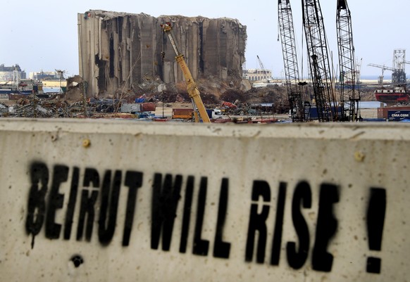 A slogan is painted on a barrier in front of towering grain silos gutted in the massive August explosion at the Beirut port that claimed the lives of more than 200 people, in Beirut, Lebanon, Wednesda ...