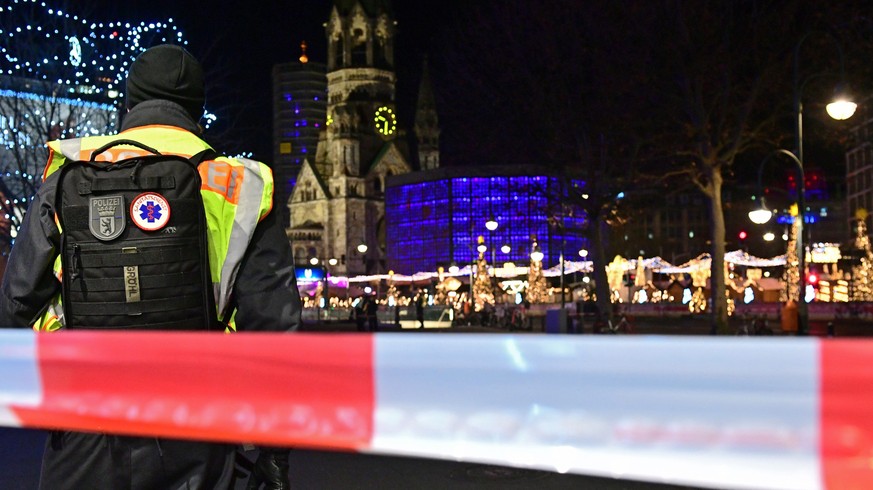 epa08085915 A policeman with a backpack reading &#039;medical service&#039; stands in front of the Kaiser-Wilhelm-Gedaechtniskirche memorial church with the Christmas market on Breitscheidplatz square ...