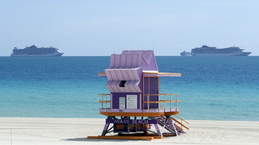Two cruise ships are anchored offshore past a lifeguard tower, Tuesday, March 31, 2020, in Miami Beach, Fla. (AP Photo/Wilfredo Lee)