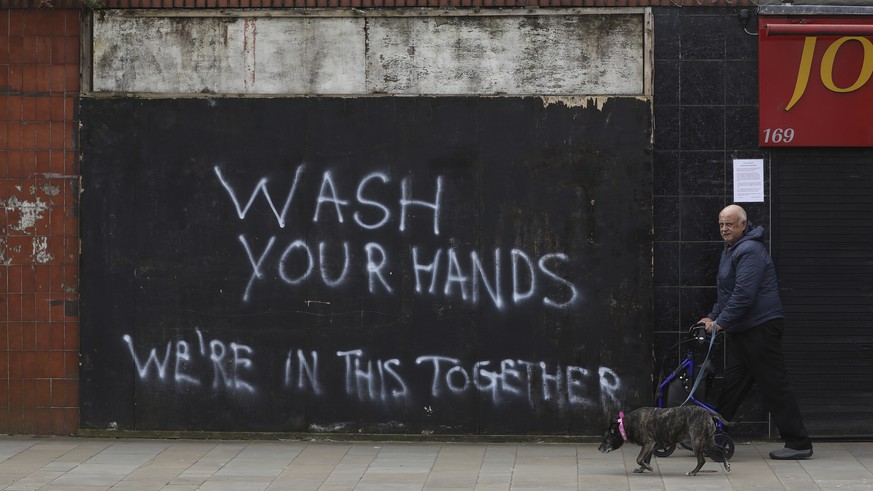 A man walks his dog past graffiti calling for people to wash their hands to combat the spread of the coronavirus, in Belfast, Northern Ireland, Monday March, 30, 2020. The new coronavirus causes mild  ...