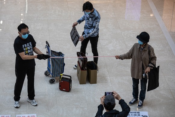 epa08381133 Demonstrators wearing face masks use a tape measurer to observe social distancing at the beginning of a protest in a shopping mall in Hong Kong, China, 24 April 2020, during the coronaviru ...