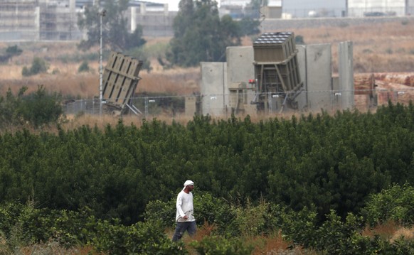 epa08568535 An Israeli farmer walks next to an Israeli Iron Dome missile defense system, designed to intercept and destroy incoming rockets and artillery shells, deployed in Hula Valley, North Israel  ...