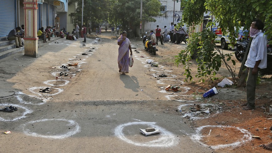 An Indian woman walks past circles drawn on the ground for maintaining social distance in a queue to receive free rice distributed at a government store during lockdown to prevent the spread of new co ...