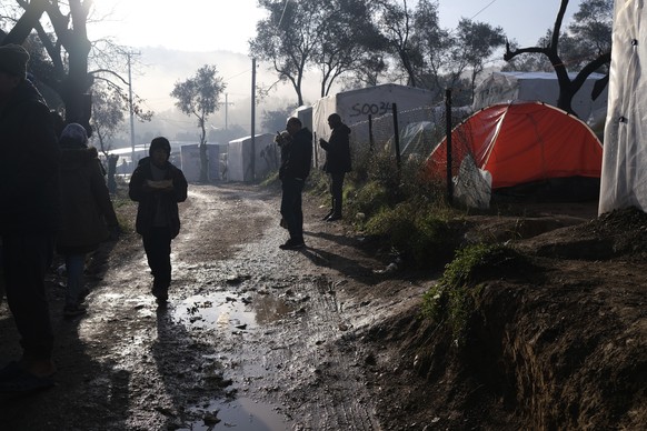 Migrants stand outside their makeshift tents outside the perimeter of the overcrowded Moria refugee camp after a rainfall on the northeastern Aegean island of Lesbos, Greece, on Tuesday, Jan. 28, 2020 ...