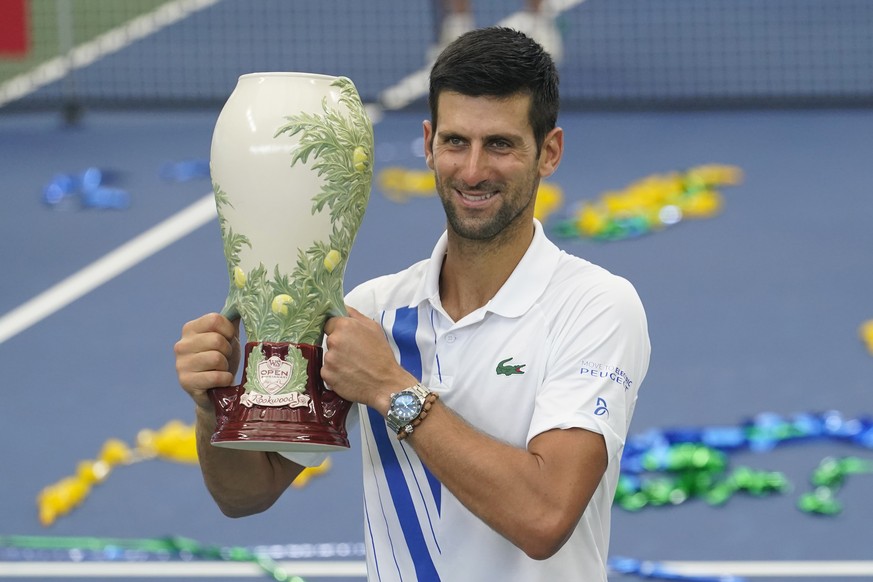 Novak Djokovic, of Serbia, front, holds his winning trophy after winning his match with Milos Raonic, of Canada, at the Western &amp; Southern Open tennis tournament Saturday, Aug. 29, 2020, in New Yo ...