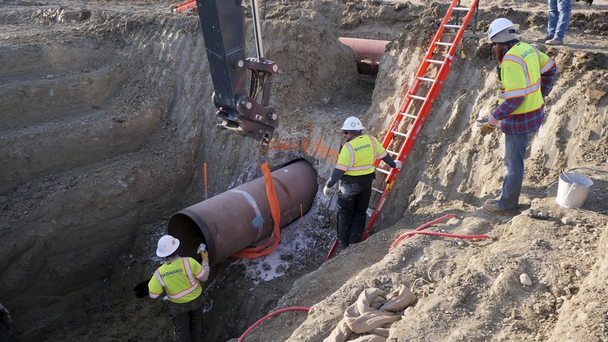 This April 13, 2020 photo provided by TC Energy shows workers for TC Energy installing a section of the Keystone XL crude oil pipeline at the U.S.-Canada border north of Glasgow, Mont. Two people work ...
