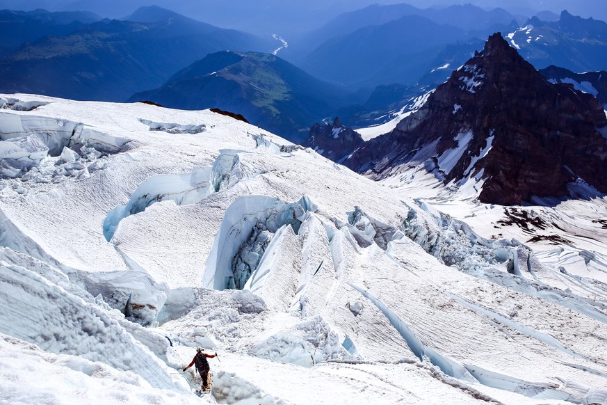 In this June 30, 2015 photo, a climber navigates a ladder placed over a crevasse high on the Ingraham Glacier during a climb of Washington&#039;s Mount Rainier. The glacier-covered faces of Mount Rain ...