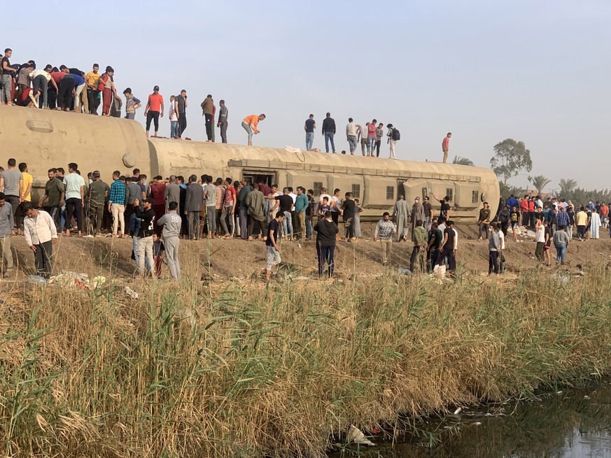 epa09143704 People stand near damaged carriages of a passenger train that was derailed in Toukh, Al Qalyubia Governorate, north of Cairo, Egypt, 18 April 2021. According to the ministry of health, 97  ...