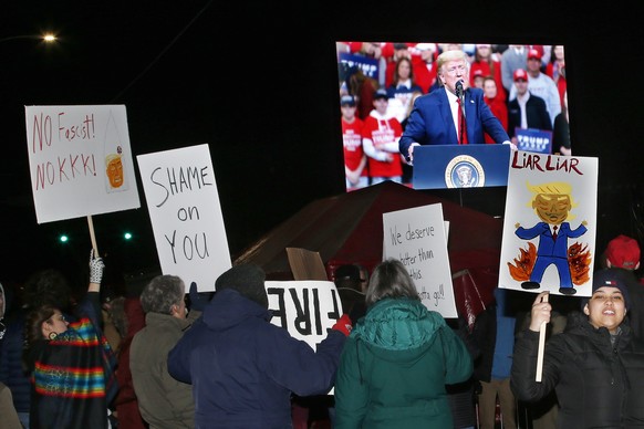 Protesters hold signs as feed of the rally is displayed on a monitor outside the campaign rally for President Donald Trump, Thursday, Jan. 30, 2020, in Des Moines, Iowa. (AP Photo/Sue Ogrocki)