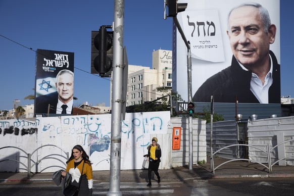 FILE - In this March. 1, 2020 file photo, people walk next to election campaign billboards showing Israeli Prime Minister Benjamin Netanyahu, right, and Benny Gantz, left, in Bnei Brak, Israel. Israel ...