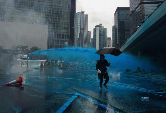 A protestor runs for cover as police fire blue-colored water from water cannons in Hong Kong, Saturday, Aug. 31, 2019. Large crowds of protesters are gathering and marching in central Hong Kong as pol ...