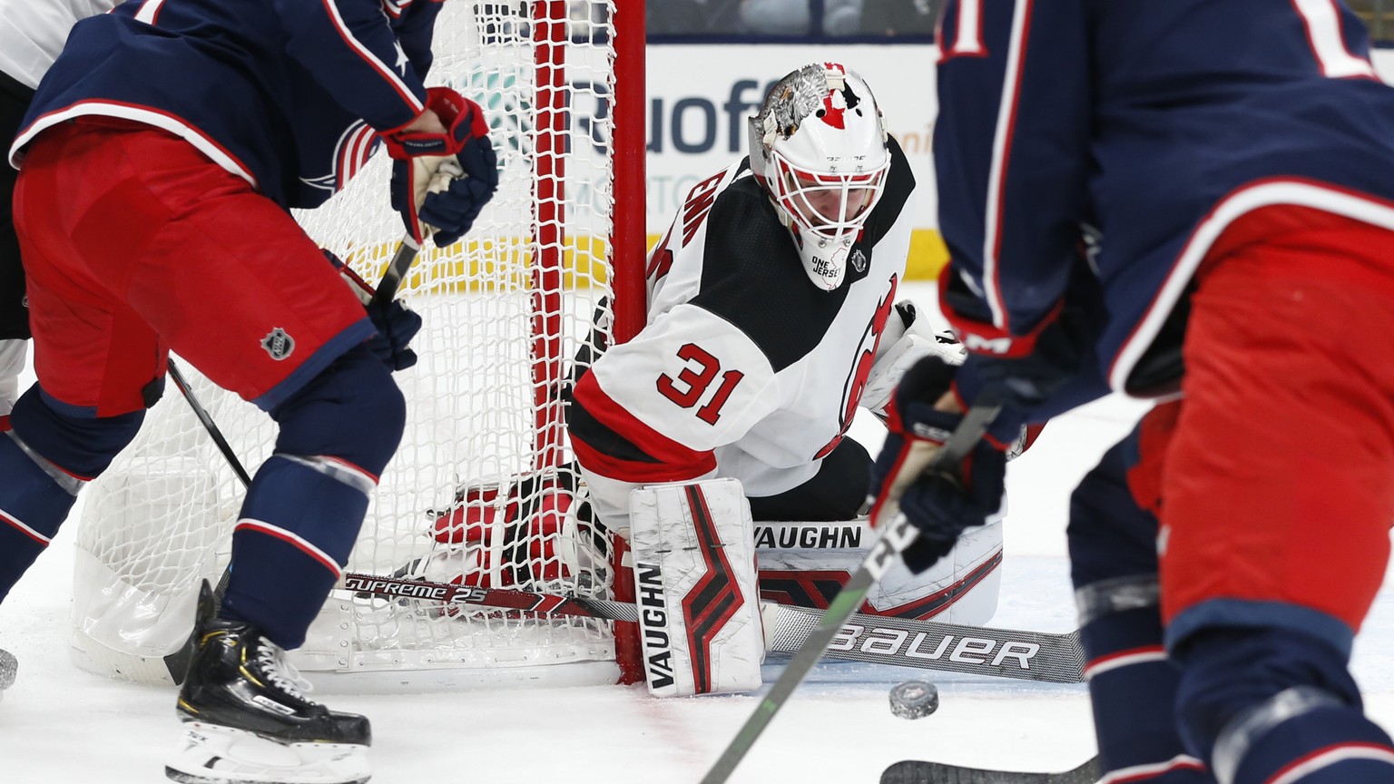 New Jersey Devils&#039; Gilles Senn, center, of Switzerland, makes a save between Columbus Blue Jackets&#039; Nick Foligno, left, and Kevin Stenlund, of Sweden, during the second period of an NHL hock ...