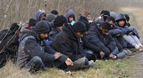 epa05151245 Detained migrants who arrived via Serbia sit near the border village of Roszke, Hungary, 09 February 2016. A group of 24 migrants from Pakistan, India and Nepal were detained by police aft ...