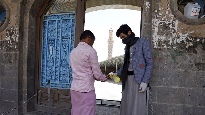 epa08341281 A Yemeni (R) disinfects the hands of a man before entering a mosque for the weekly Friday prayers in Sanaa, Yemen, 03 April 2020. Countries around the world implemented measures to stem th ...