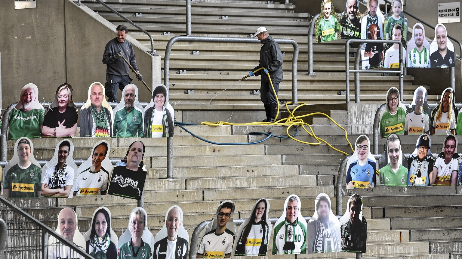 Workers clean the supporters tribune where portraits of fans of German Bundesliga soccer club Borussia Moenchengladbach are set in the stadium in Moenchengladbach, Germany, Thursday, April 16, 2020. A ...