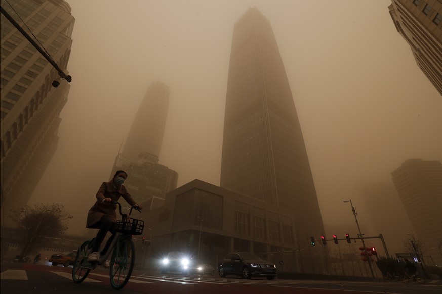 A cyclist and motorists move past office buildings amid a sandstorm during the morning rush hour in the central business district in Beijing, Monday, March 15, 2021. The sandstorm brought a tinted haz ...