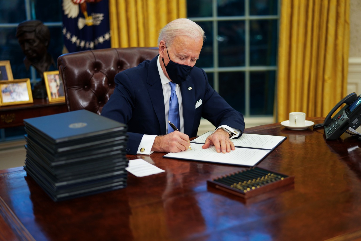 epa08954623 US President Joe Biden signs executive order on Covid-19 during his first minutes in the Oval Office, in the White House, Washington, DC, USA, 20 January 2021, following his inauguration a ...