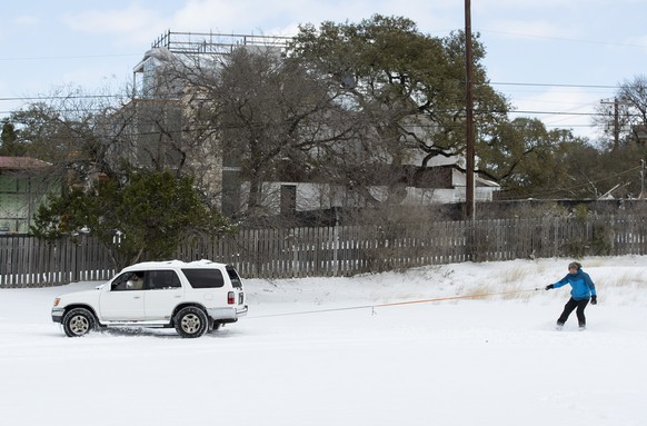 Ehsan M. rides a snowboard behind a friend&#039;s SUV in a parking lot in Travis Heights after a heavy snow on Monday Feb. 15, 2021. (Jay Janner /Austin American-Statesman via AP)