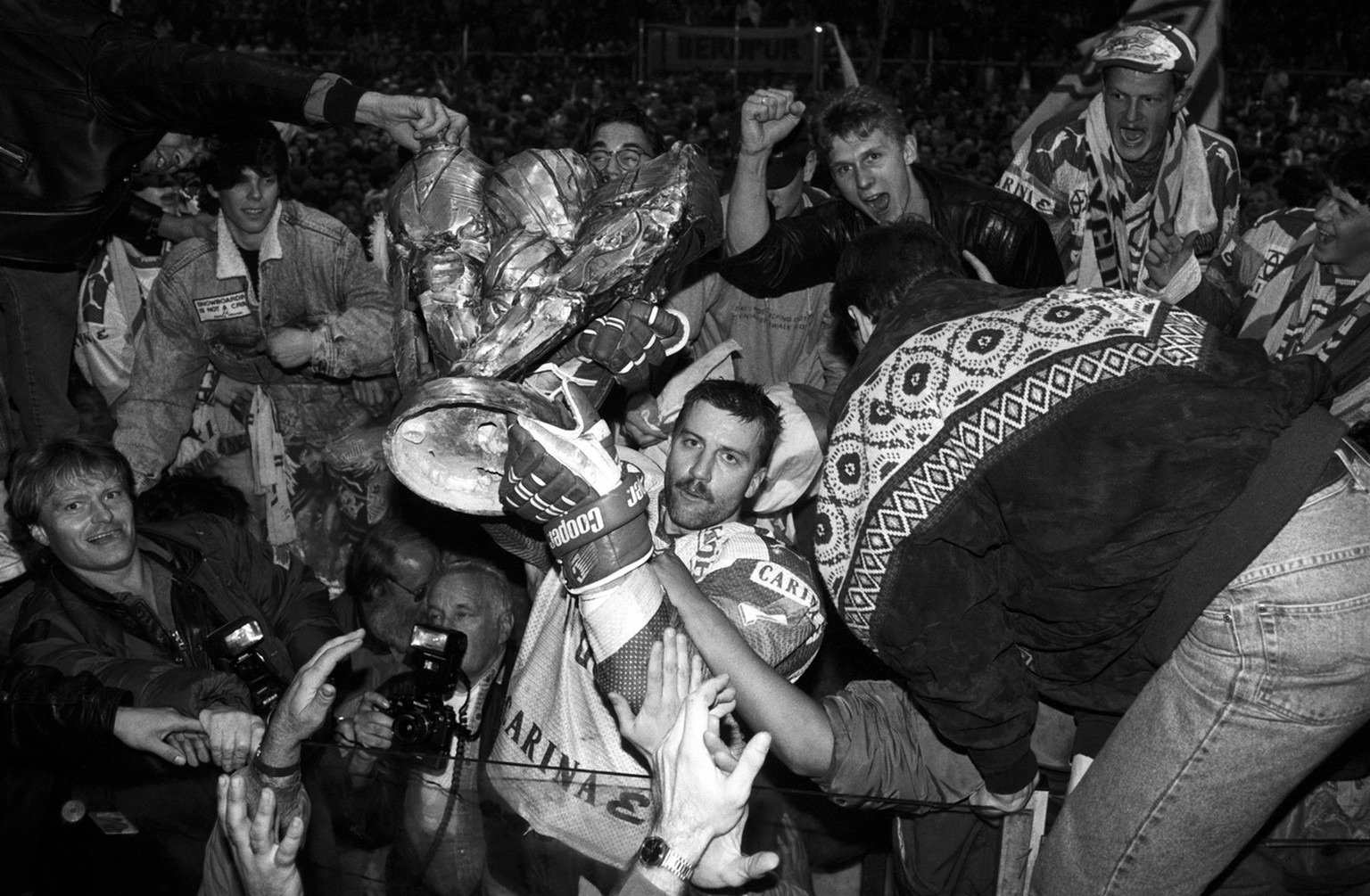 Der Eishockeyspieler Peter Schlagenhauf vom EHC Kloten und andere Mitglieder der Mannschaft und Fans feiern am 23. Maerz 1993 mit dem Meisterpokal den Gewinn der Schweizermeisterschaft. Links am Bildr ...