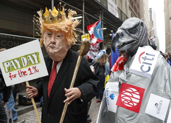 A man dressed as President Donald Trump holds a golf club as he stands beside a person dressed as a corporate vulture during a May Day rally in front of 40 Wall Street, a Trump-owned property, Wednesd ...