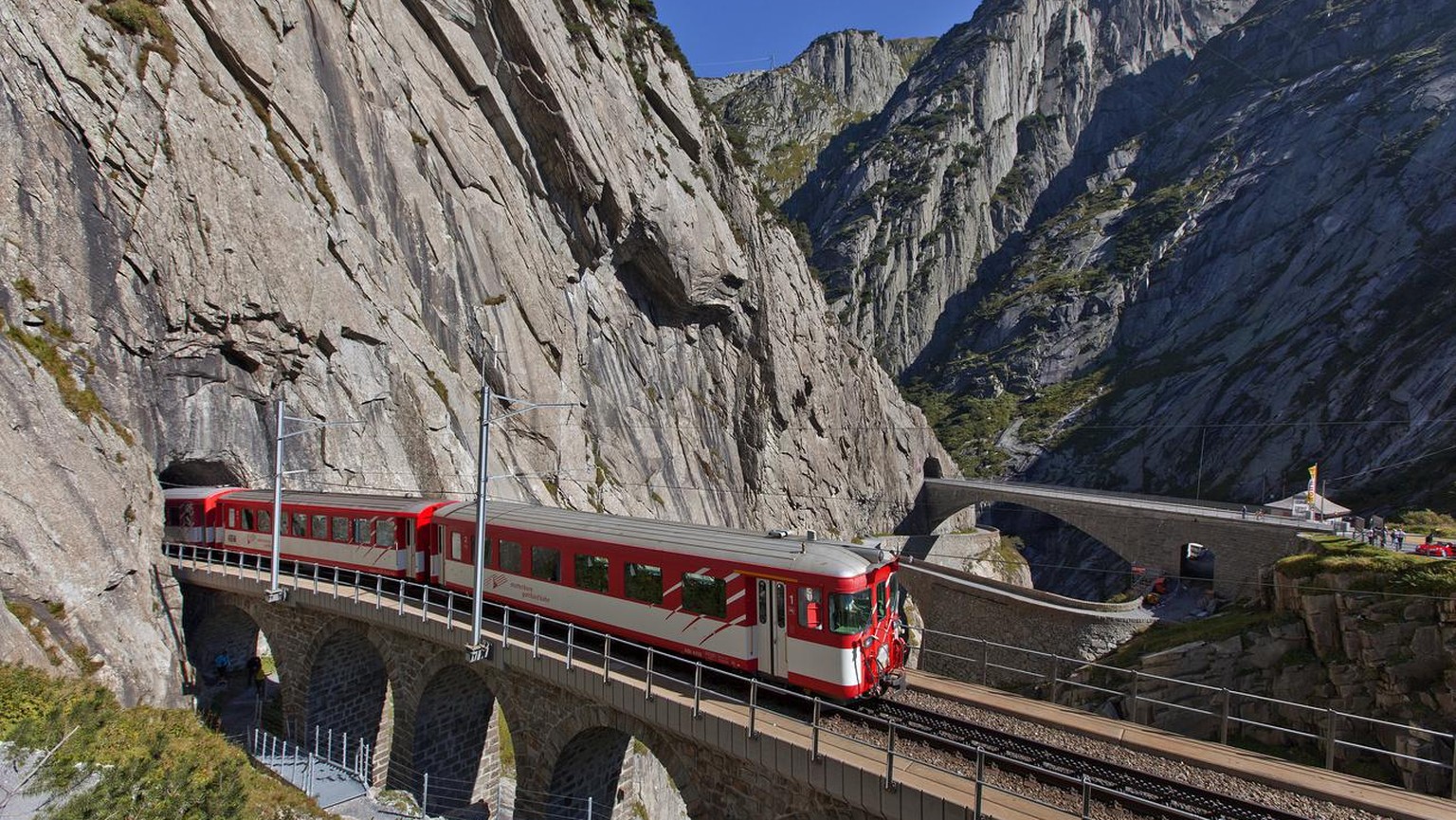 The Matterhorn Gotthardbahn, a meter-gauge railroad, driving over the so called Teufelsbruecke, &quot;Devil&#039;s bridge&quot;, in the gorge Schoellenenschlucht and the river Reuss. canton of Uri, Sw ...