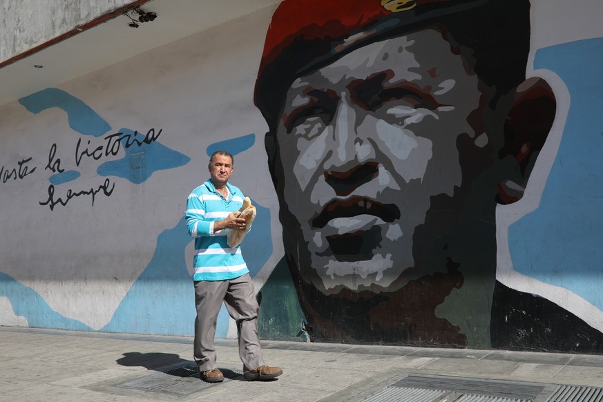 A man walks with a couple loaves of bread past a mural of Venezuela&#039;s late former president Hugo Chavez, in Caracas, Venezuela, Tuesday, Feb. 12, 2019. Nearly three weeks after the Trump administ ...