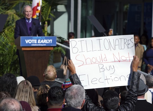 A protestor holds up a sign as presidential candidate Michael Bloomberg speaks at a campaign event at the Dollarhide Community Center in Compton, Calif., Monday, Feb. 3, 2020. Bloomberg kicked off his ...