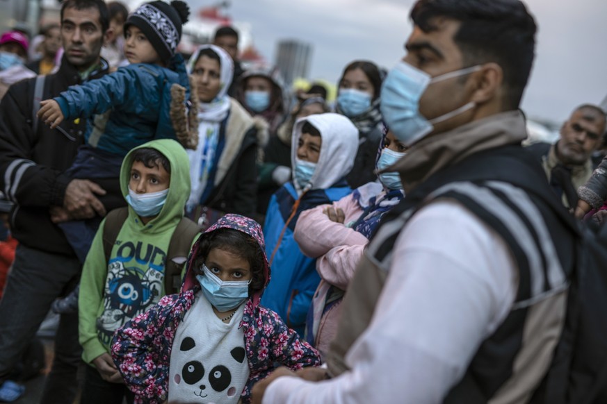Refugees and migrants wearing masks to prevent the spread of the coronavirus, wait to get on a bus after their arrival at the port of Piraeus, near Athens on Monday, May 4, 2020. Greek authorities are ...
