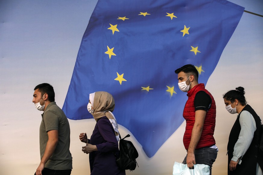FILE - In this Tuesday, June 2, 2020 file photo, people walk past a poster of a European Union flag in Istanbul. Following the approval of European leaders Friday Dec. 11 of expanding sanctions agains ...