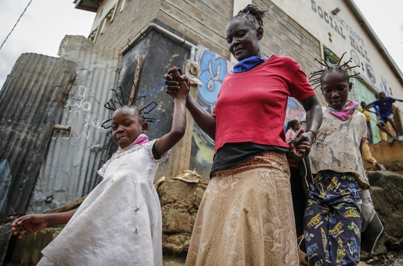 FILE - In this Sunday, May 3, 2020 file photo, Margaret Andeya takes her daughter Gettrueth Ambio, 12, right, and her neighbor&#039;s daughter Jane Mbone, 7, left, back home after having their hair st ...