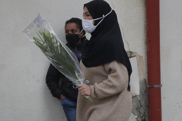 A girl holds a flower to lay at the entrance of the school where a slain history teacher was working, Saturday, Oct. 17, 2020 in Conflans-Sainte-Honorine, northwest of Paris. French President Emmanuel ...