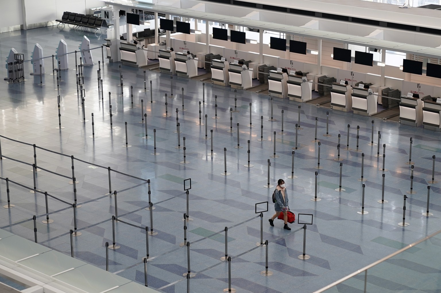 epa08305664 A passenger walks through an emptied check-in area at Haneda International Airport in Tokyo, Japan, 19 March 2020. According to government data, with a 58 percent plunge following the coro ...