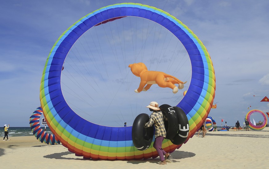 In this Sunday, June 11, 2017 photo, a woman carrying lifebuoy rubber ties walks past flying kites on Tam Thanh beach during an International Kite Festival in Quang Nam province, Vietnam. Hundreds of  ...