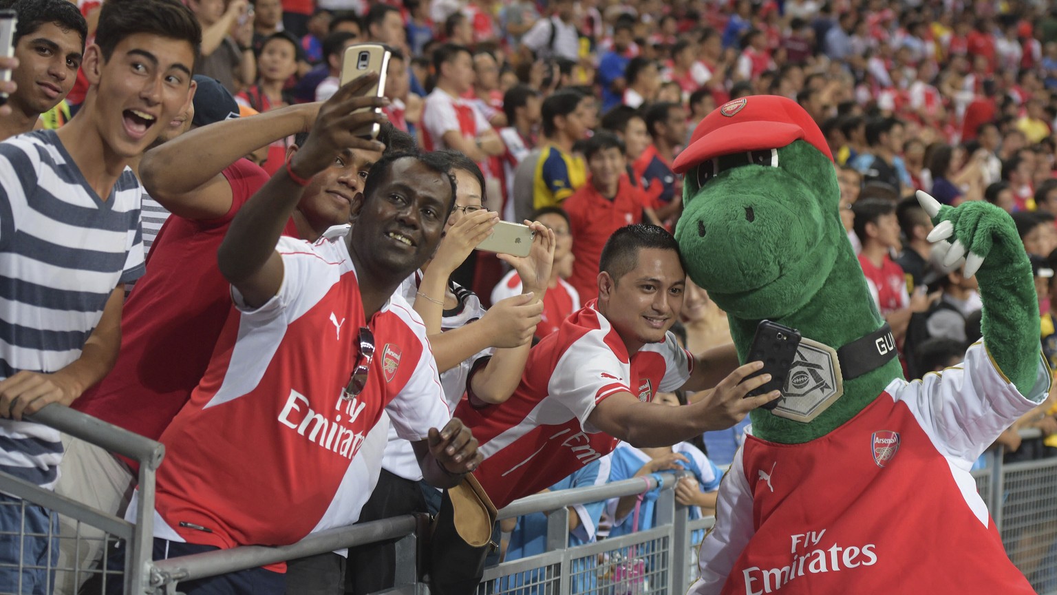 FILE - In this Saturday, July 18, 2015 file photo, fans pose for pictures with Arsenal&#039;s mascot Gunnersaurus ahead of their team&#039;s soccer match against Everton for the Barclays Asia Trophy i ...