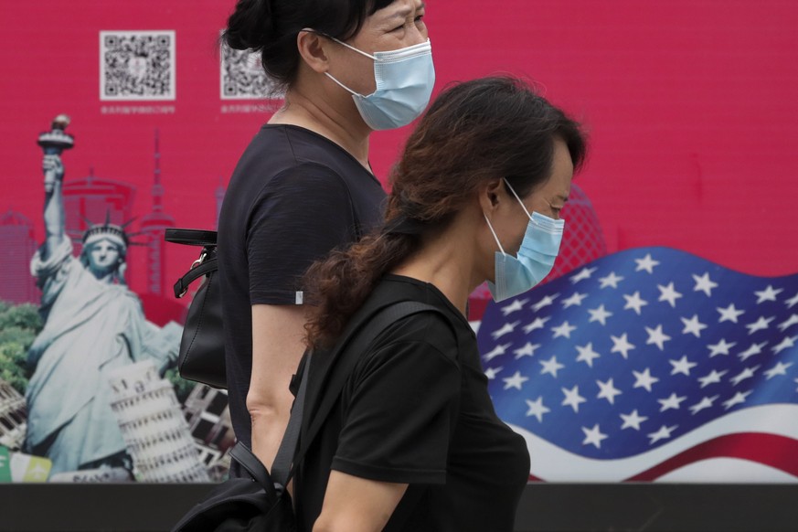 Women wearing face masks to help protect against the coronavirus walks by an advertising board displaying an American flag and Statue of Liberty on a street in Beijing, Thursday, Aug. 6, 2020. China&# ...