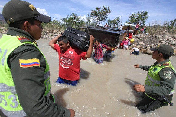 Kolumbianische Polizisten geleiten ihre Staatsbürger durch den Fluss über die Grenze.