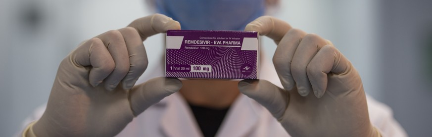 epa08508728 An employee wears a face mask and holds up a box of remdesivir while posing for a photograph at the laboratories of the Eva Pharma company in Cairo, Egypt, 25 June 2020. The Egyptian drugm ...